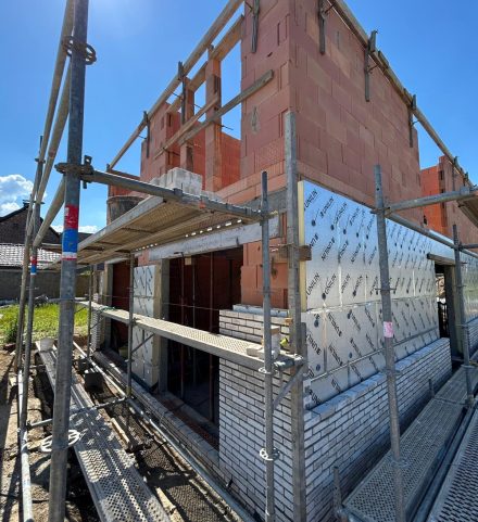 Een close-up van de hoek van een huis in aanbouw, waarbij de bakstenen en isolatiepanelen benadrukken dat er veel administratie komt kijken bij de bouw