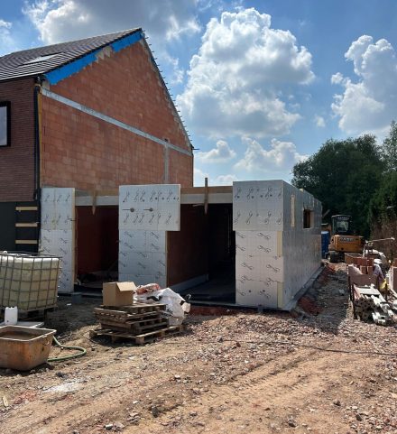 Een onafgewerkt huis in opbouw, met isolatie en bakstenen, symboliseert de start van een bouwproject en de bijbehorende administratie
